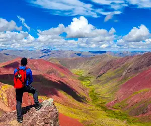 Turista posando en el Valle Rojo, con un cielo azul y nubes blancas.
